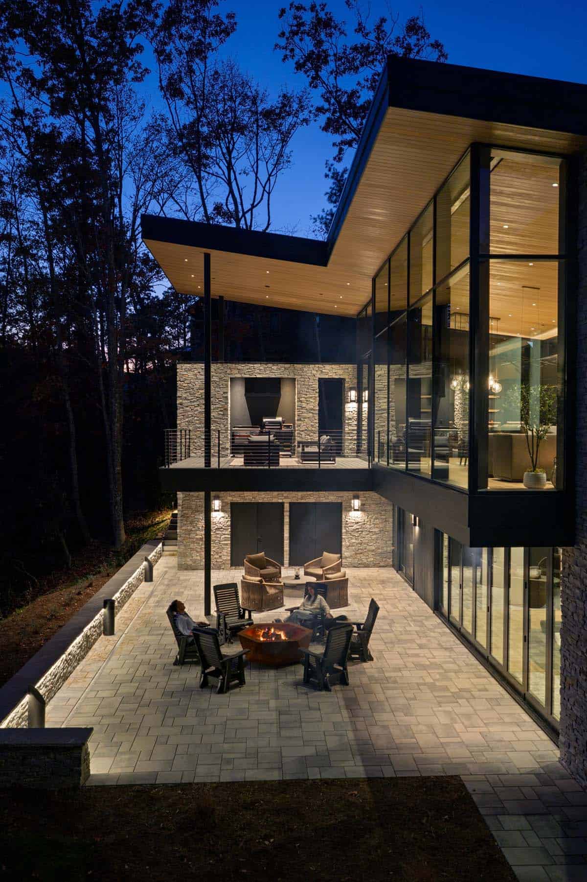 Aerial view of home's stone patio with fire pit seating under dramatic roof overhang at dusk
