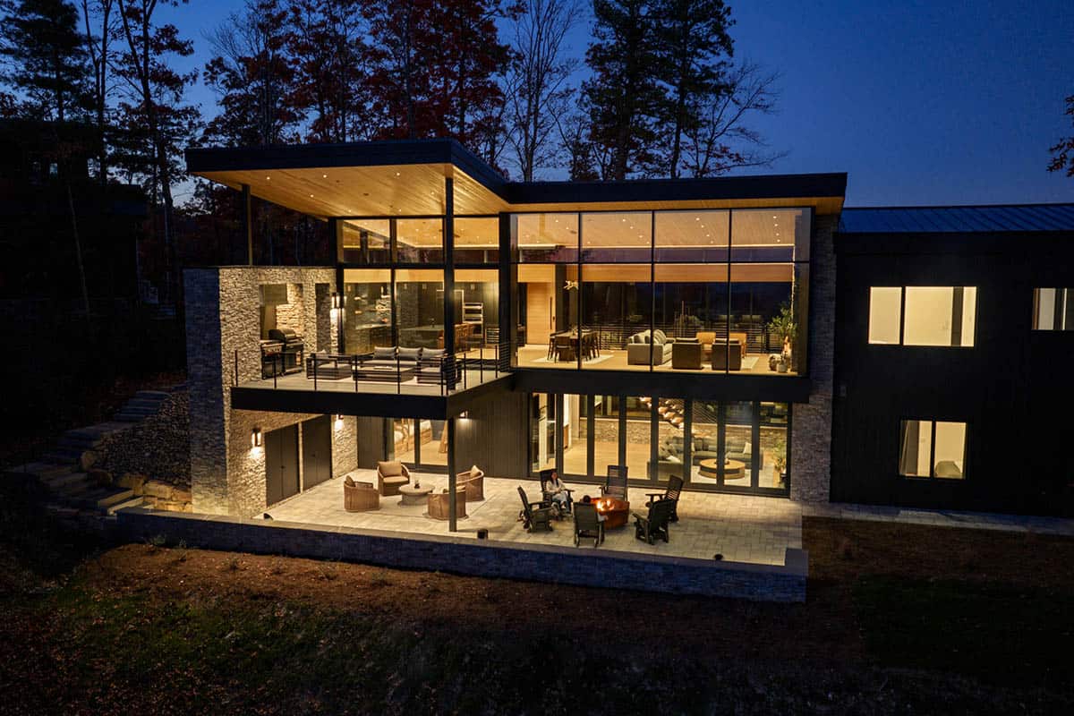 Two-story home exterior at dusk with glowing interior and outdoor fire pit gathering