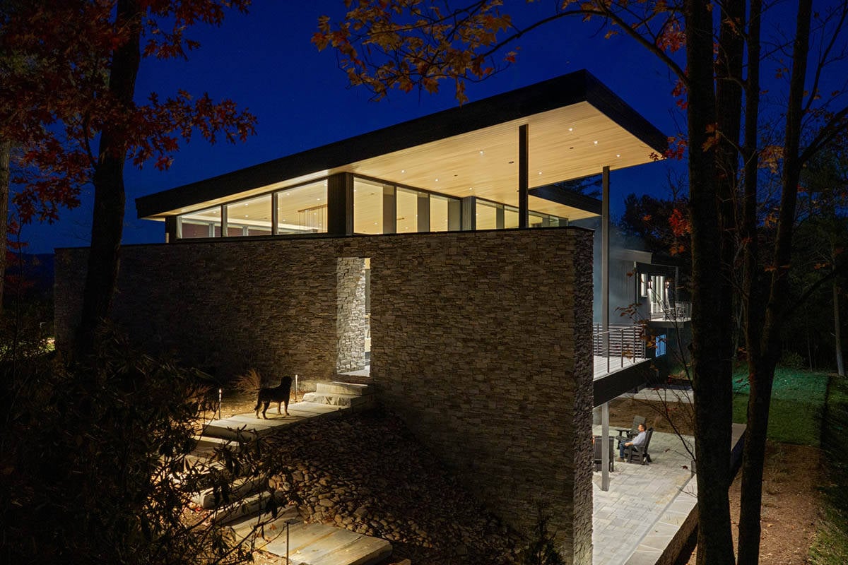 Stone facade of home with dog on steps and lit deck seating at night
