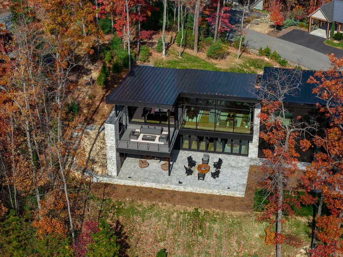 Bird's-eye aerial view of modern home with dark roof nestled among colorful fall trees