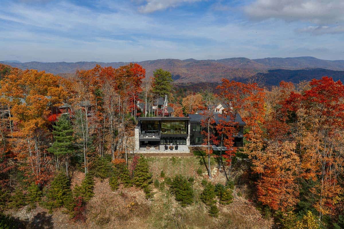 Aerial view of glass-walled home framed by dense fall foliage overlooking distant mountains
