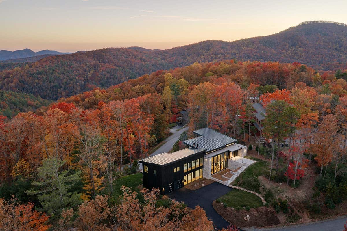 Aerial view of illuminated home in autumn woods at sunset with mountain layers beyond