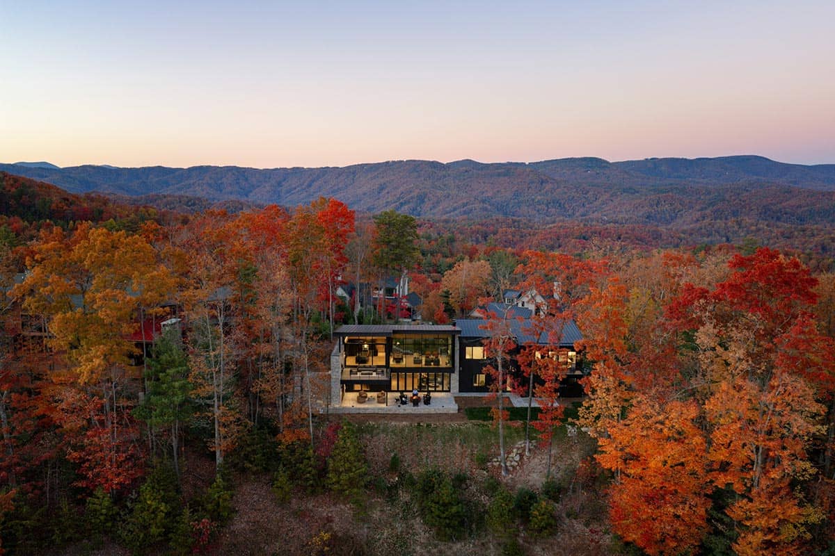Aerial view of home glowing at dusk surrounded by fall trees and mountain silhouettes