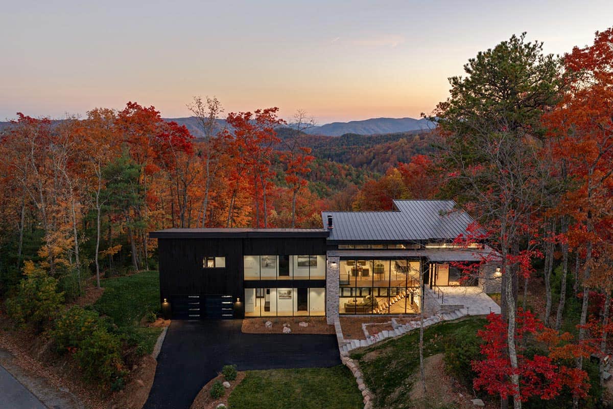 Aerial sunset view of home's dark facade and glass wall against layered mountain backdrop
