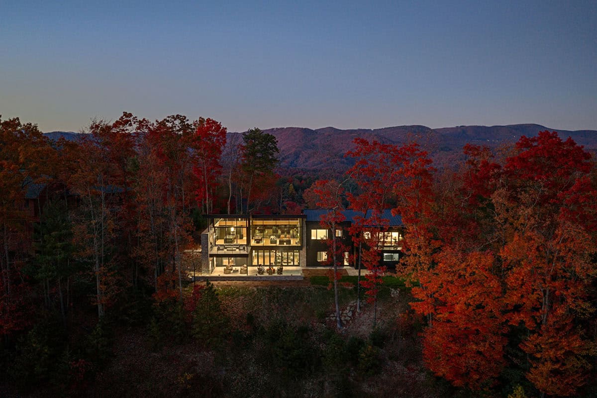 Aerial night view of glowing home surrounded by red autumn trees and dark mountain ridges