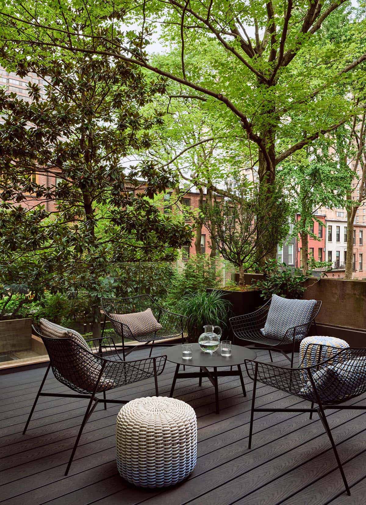 Rooftop deck of an Upper East Side brownstone with black wire chairs, woven pouf, and tree canopy