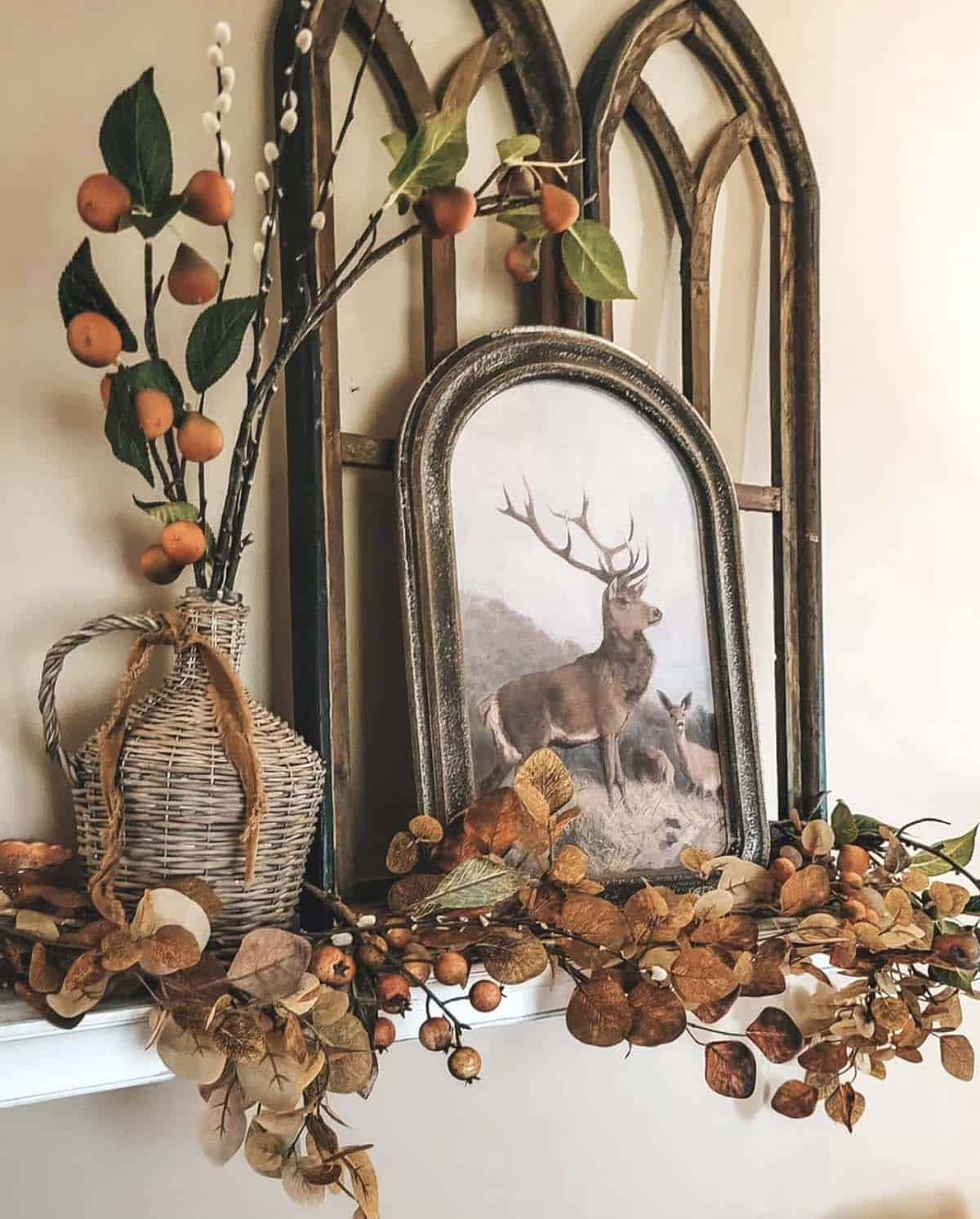 Arched wood frames with stag print above mantel draped in fall leaf garland