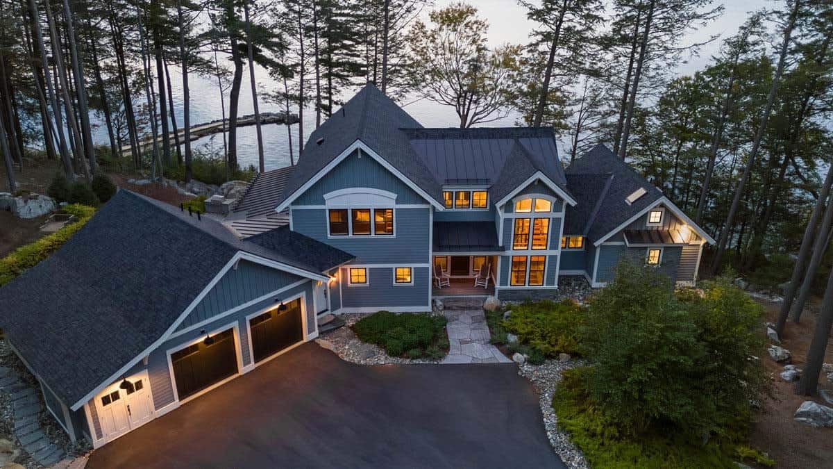 Aerial view of cottage entry, stone walkway, and lake beyond the pines