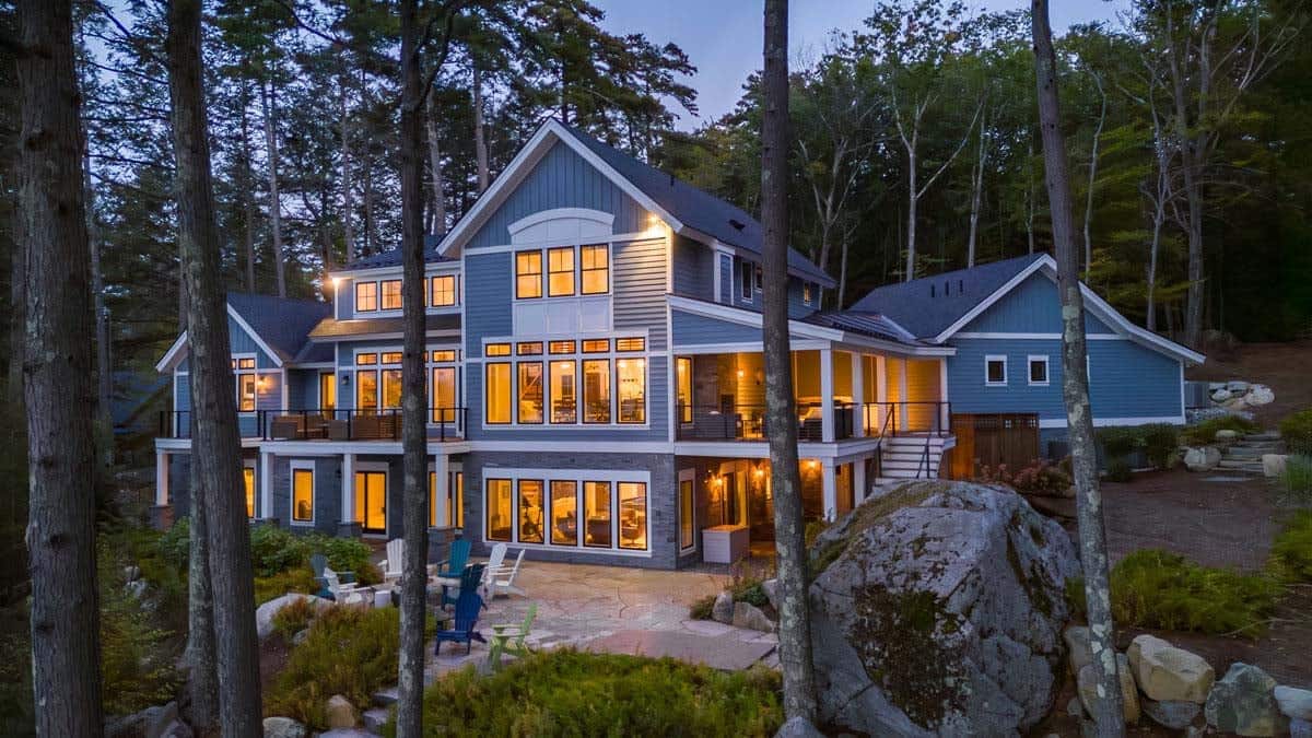Rear of lakeside cottage glowing at dusk with stone patio and boulder