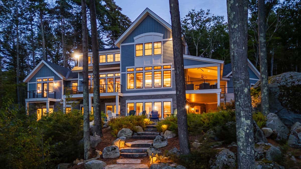 Stone steps lead up to lakefront cottage with glowing windows among pines