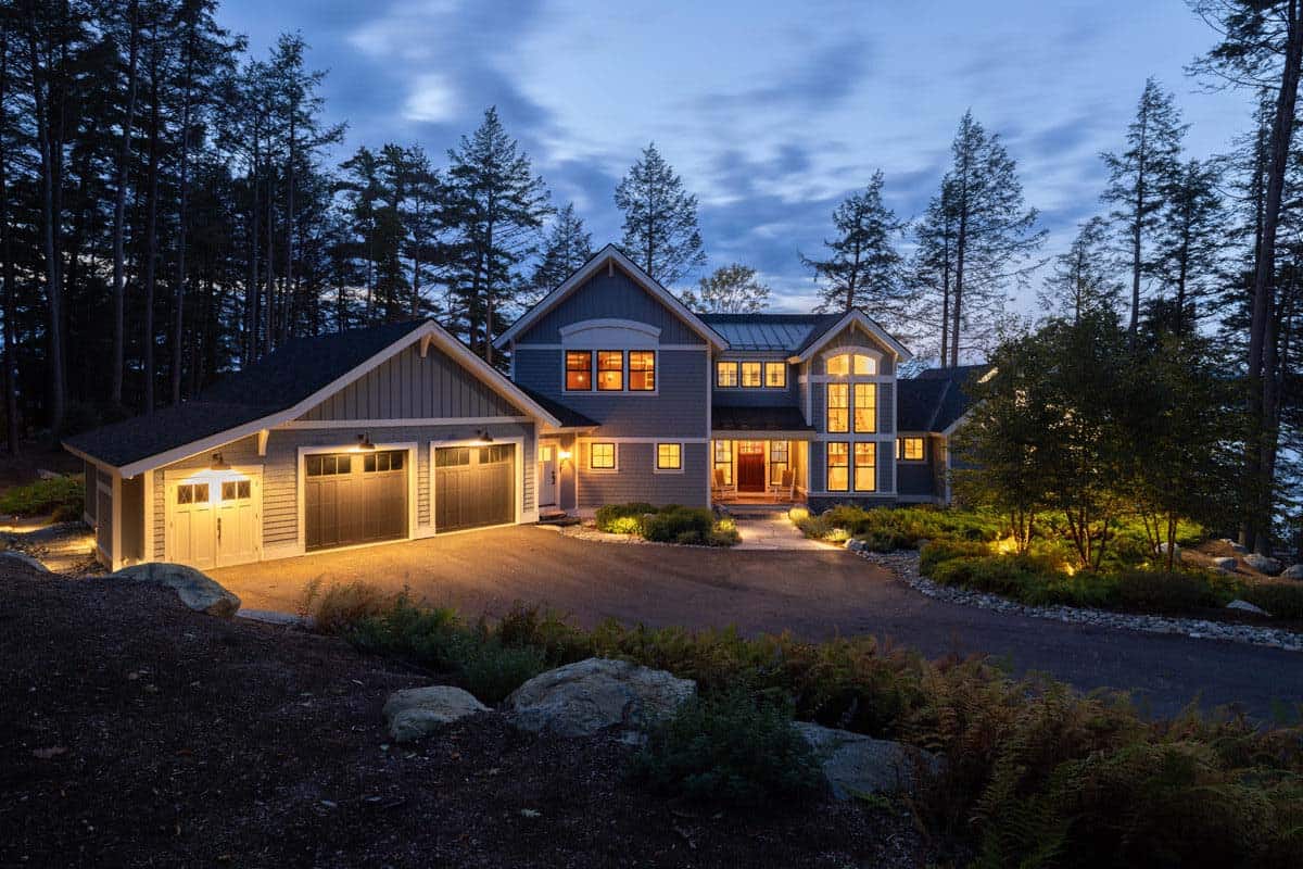 Cottage entry and garage glowing at twilight, surrounded by pines and ferns
