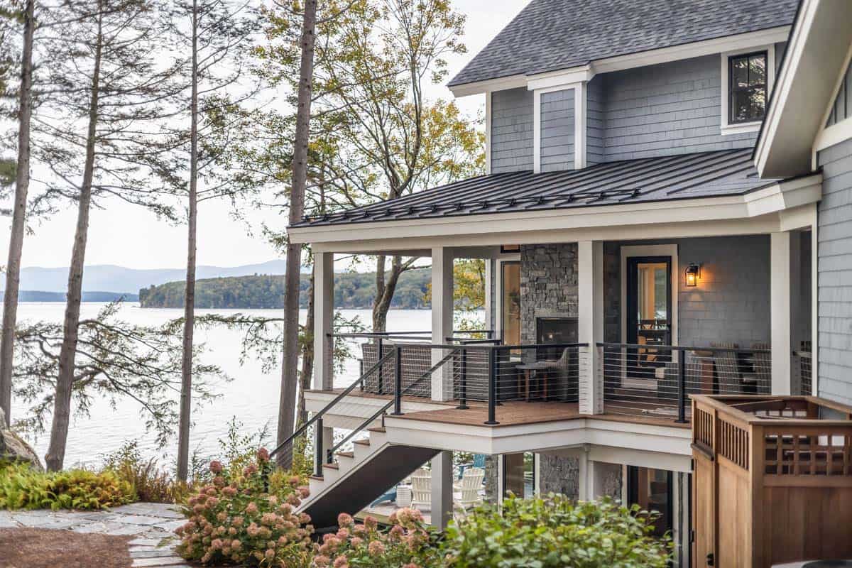 Covered lakeside porch with stone fireplace, cable railing, and mountain views