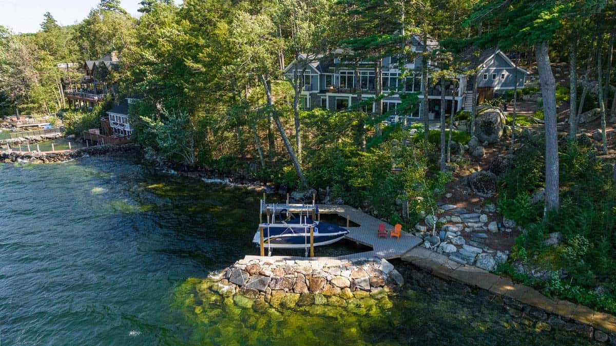 Aerial of boat dock, stone breakwater, and cottage above the shoreline