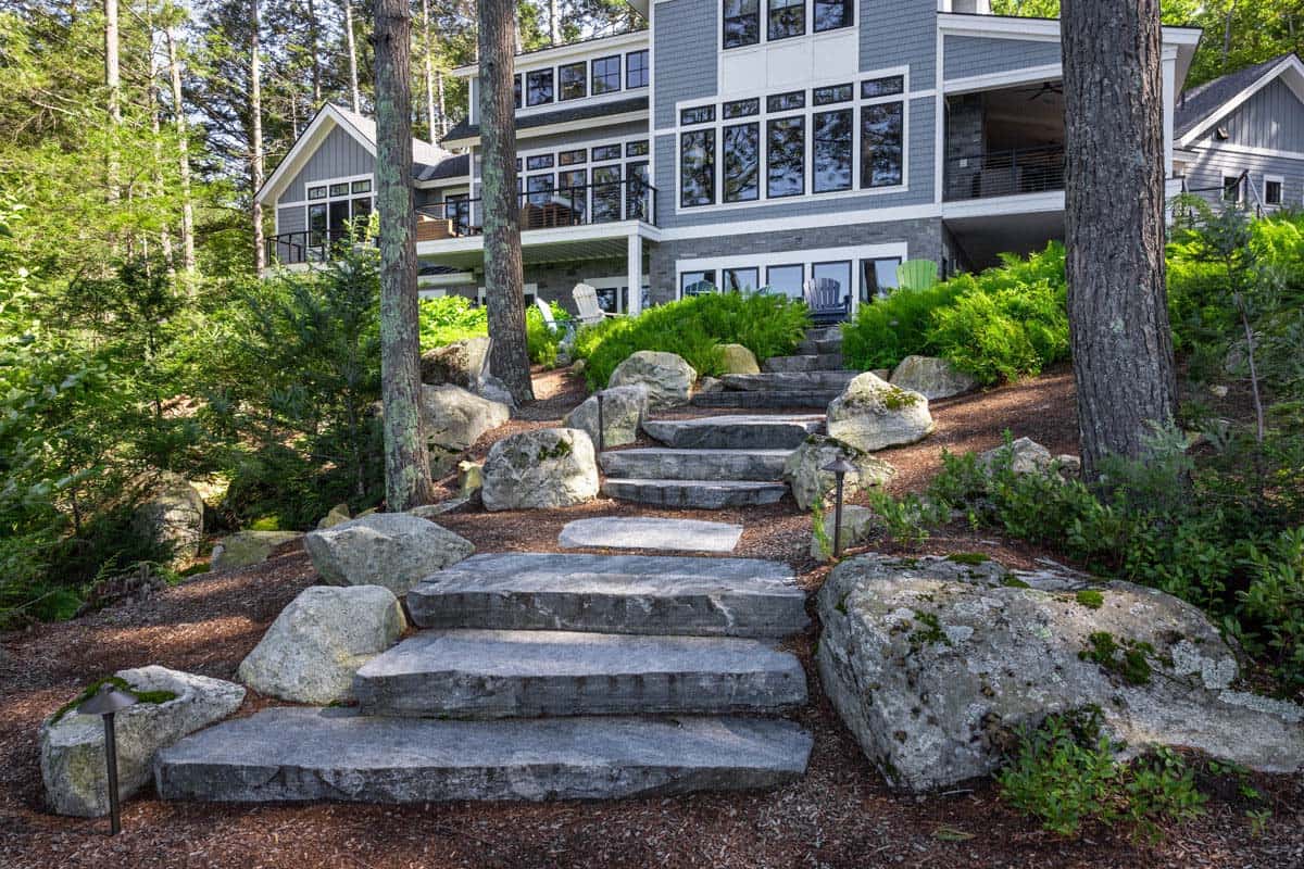 Wide granite slab steps frame view of cottage through tall pines