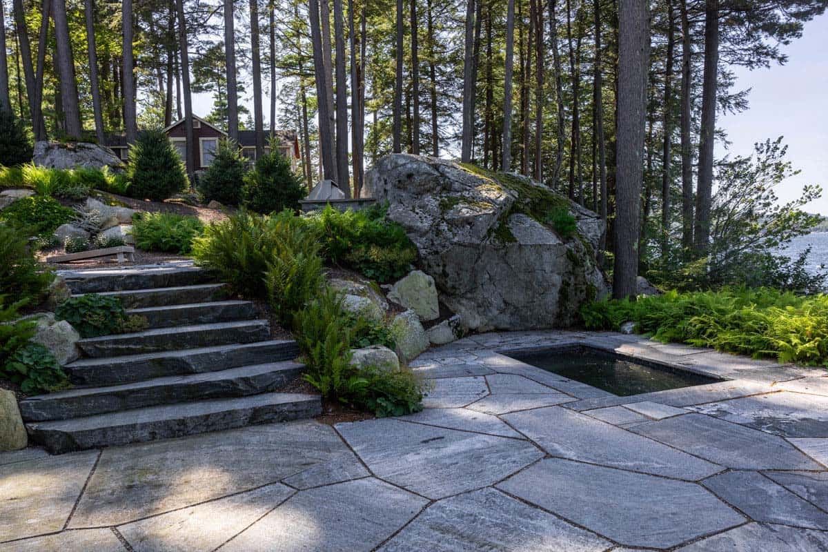 Flagstone patio, granite steps, and sunken spa tucked beside a mossy boulder