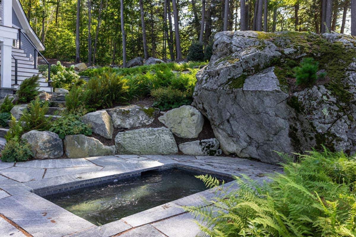 Sunken spa set into flagstone patio beside mossy boulder and ferns