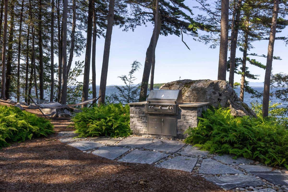 Stone outdoor grill station with boulder backdrop and hammock in the pines