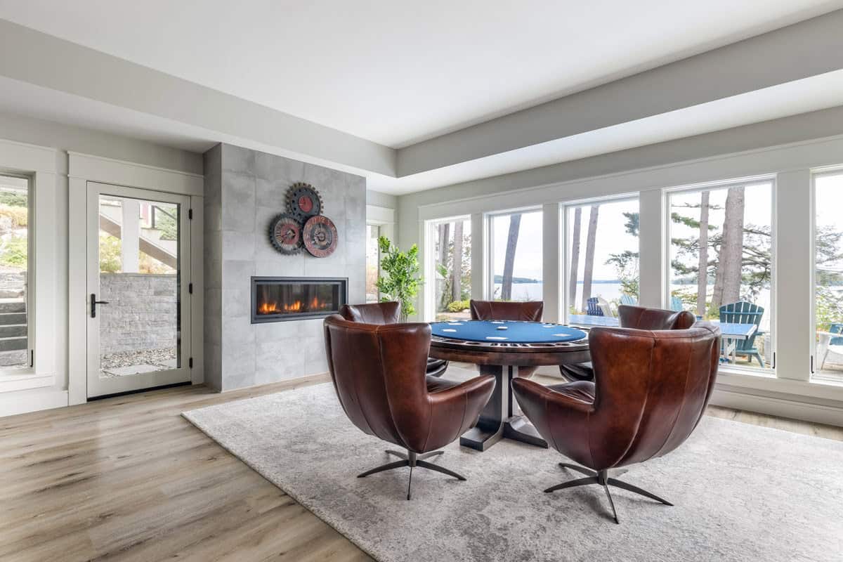 Card table with leather swivel chairs beside linear fireplace and lake windows