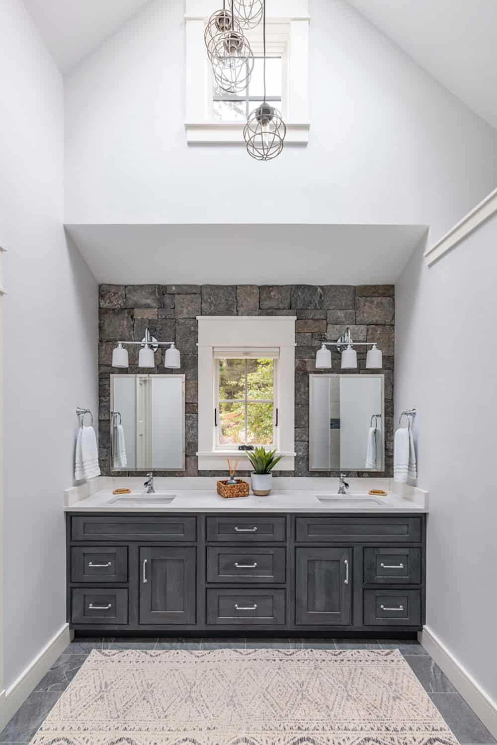 Double vanity with stone accent wall, black-framed window, and vaulted ceiling