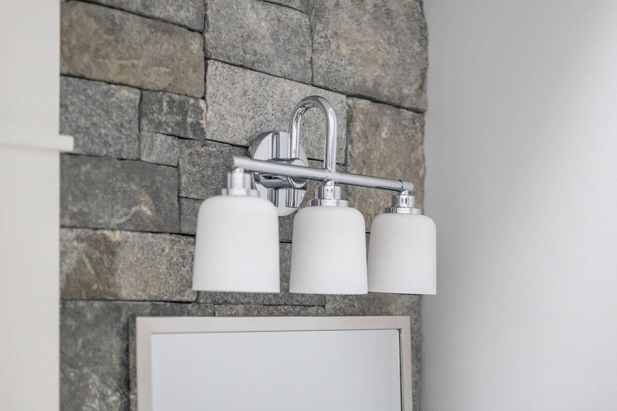 Chrome three-light vanity sconce mounted on stone accent wall above mirror