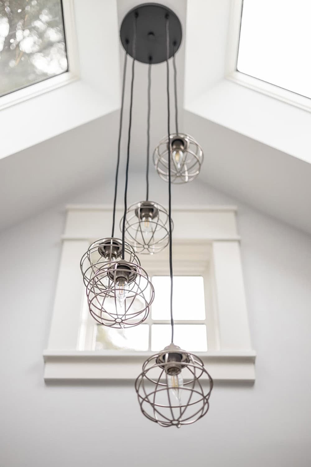 Cluster of cage pendant lights hanging beneath vaulted ceiling windows