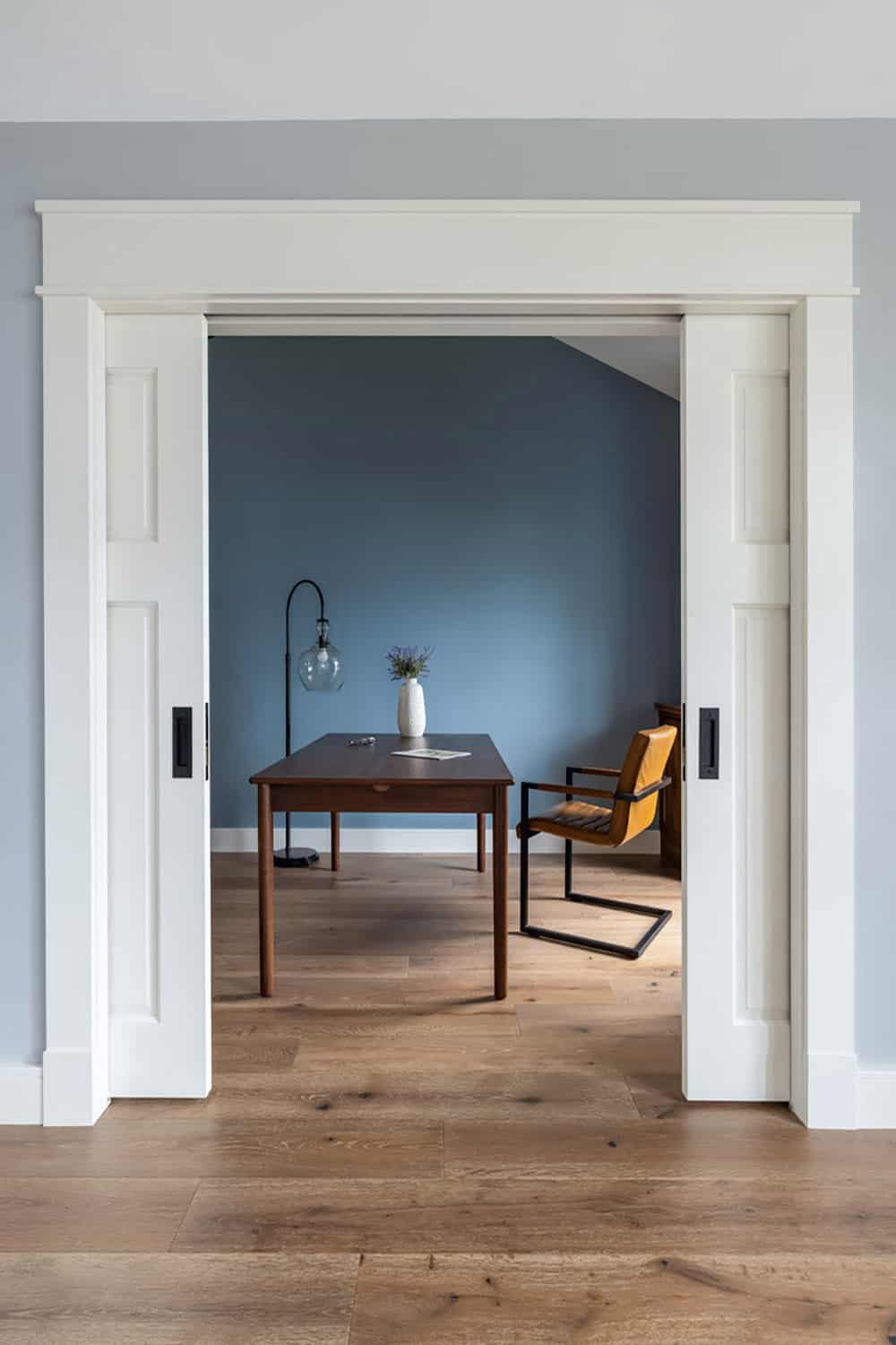 Open pocket doors reveal blue office with walnut desk and leather chair