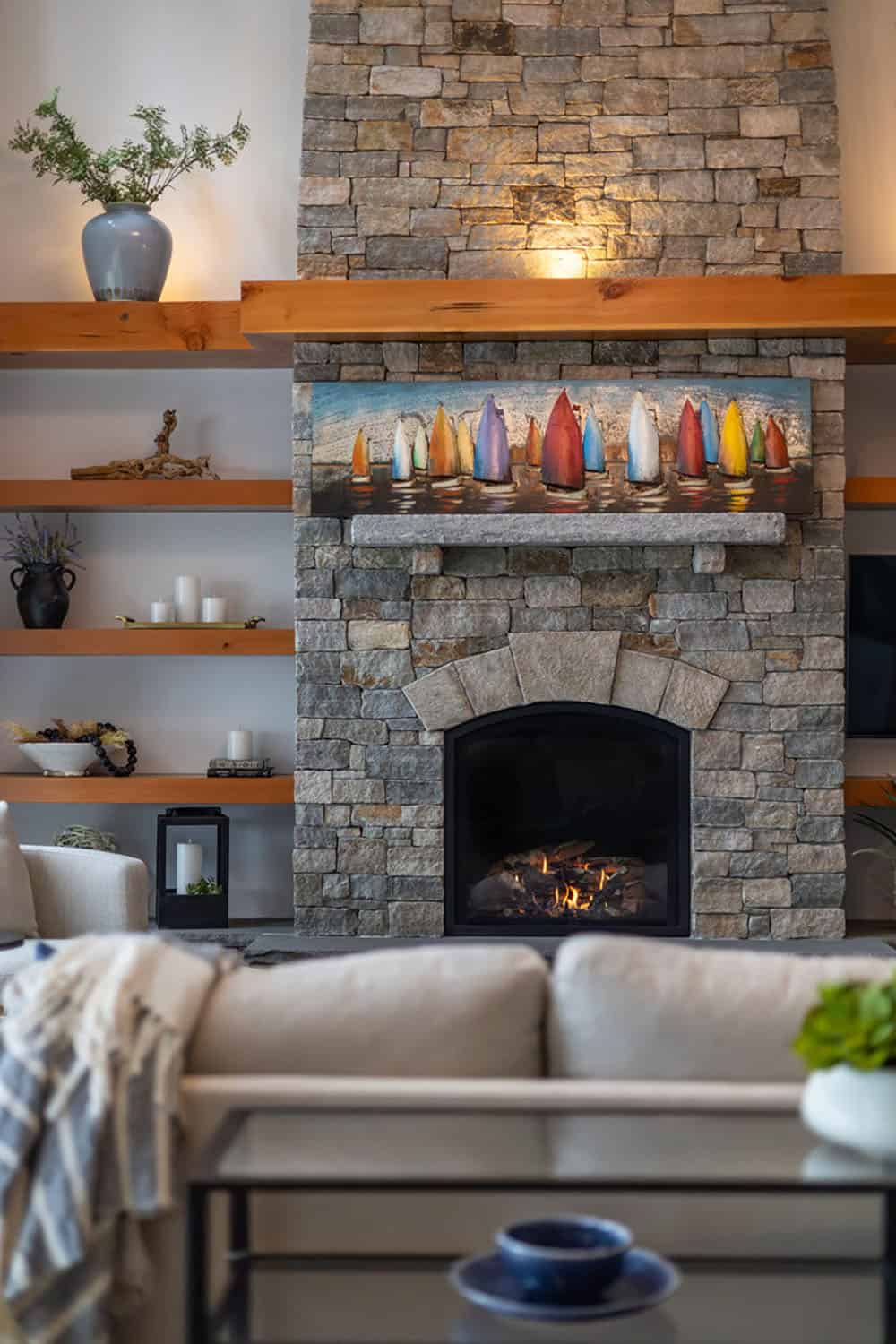 Stone fireplace with floating wood shelves and colorful sailboat artwork