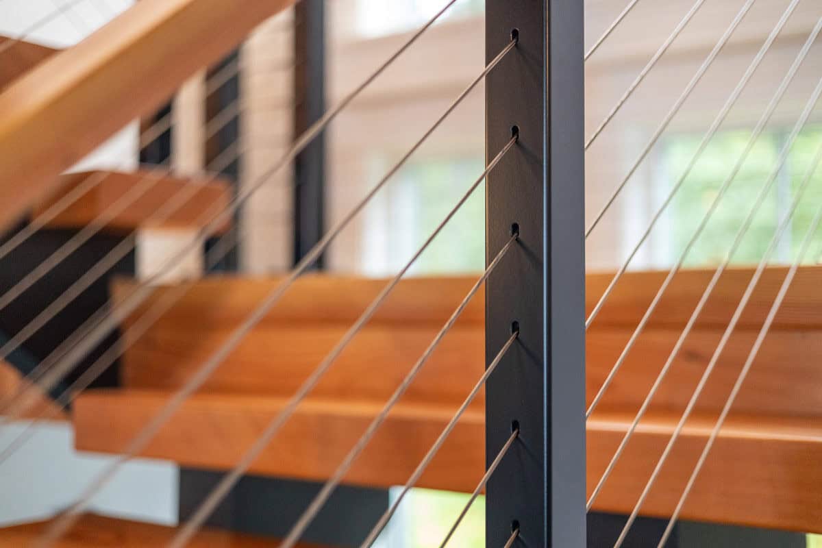 Close-up of black steel post with cable railing beside wood treads