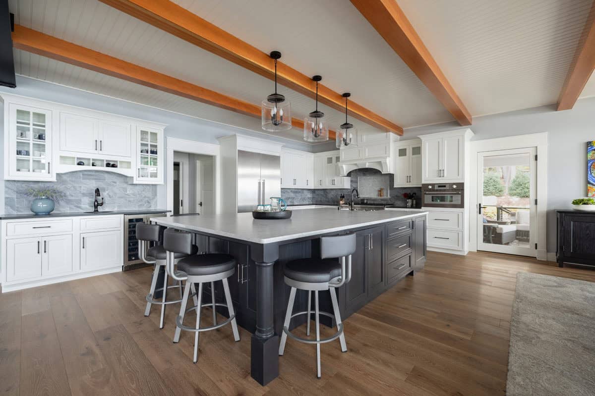 Kitchen with dark island, white cabinets, gray backsplash, and beamed ceiling