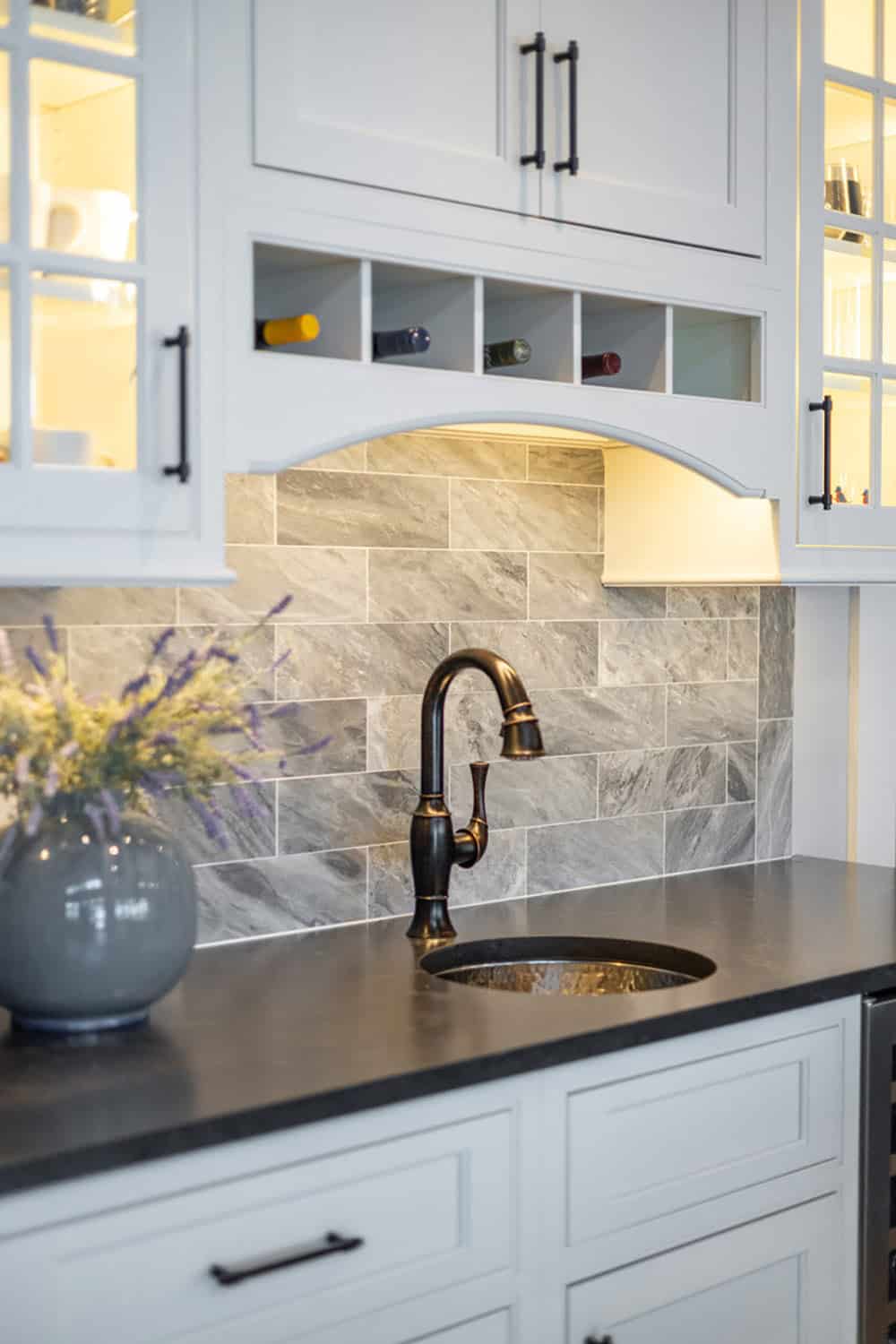 Wet bar sink with bronze faucet, gray tile backsplash, and built-in wine cubbies