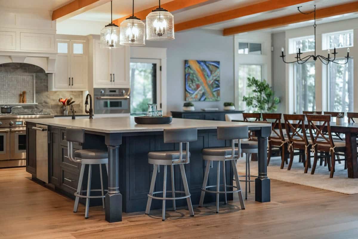 Large navy island with swivel stools beside beamed dining area