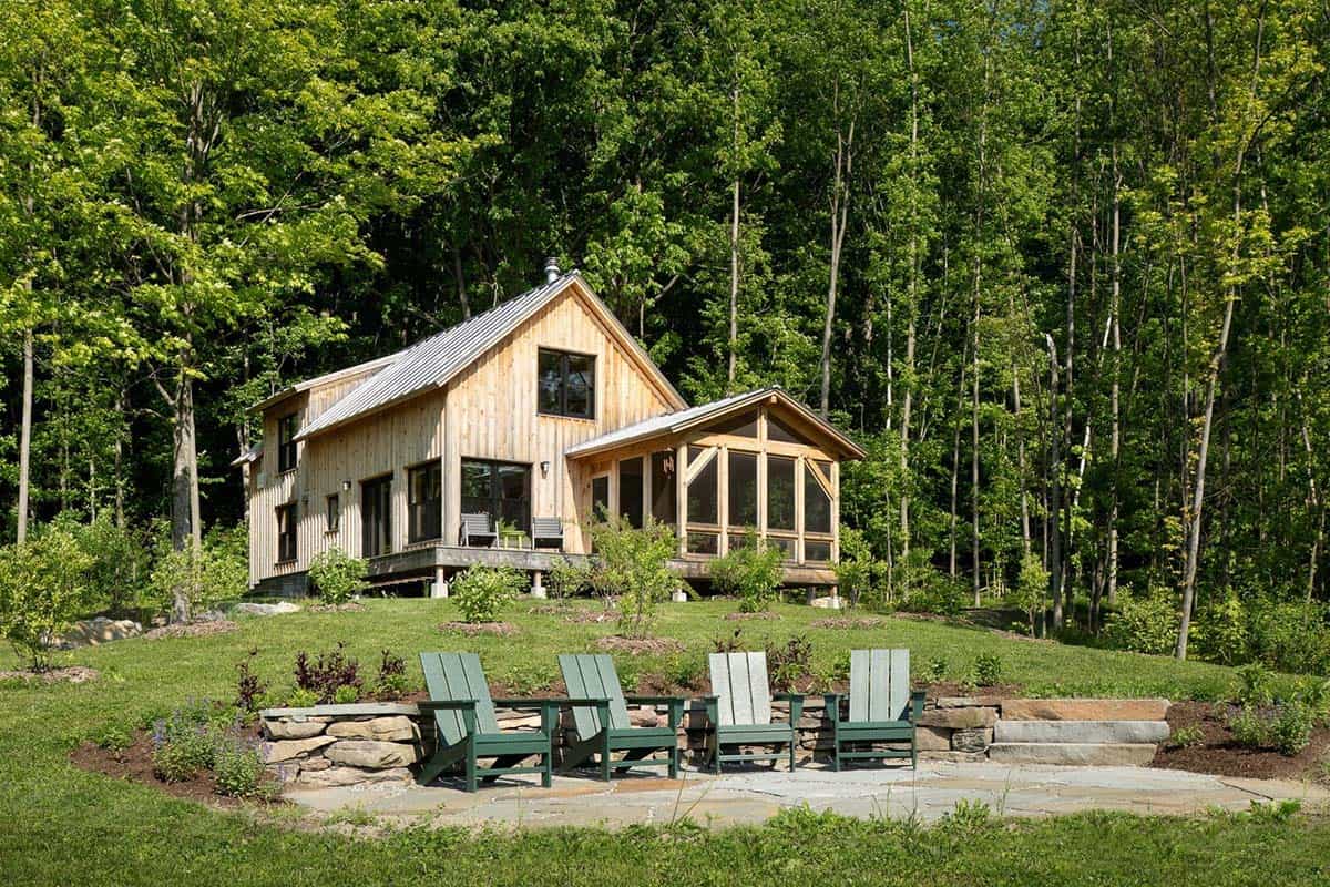Cabin on a wooded hillside with stone patio and green Adirondack chairs