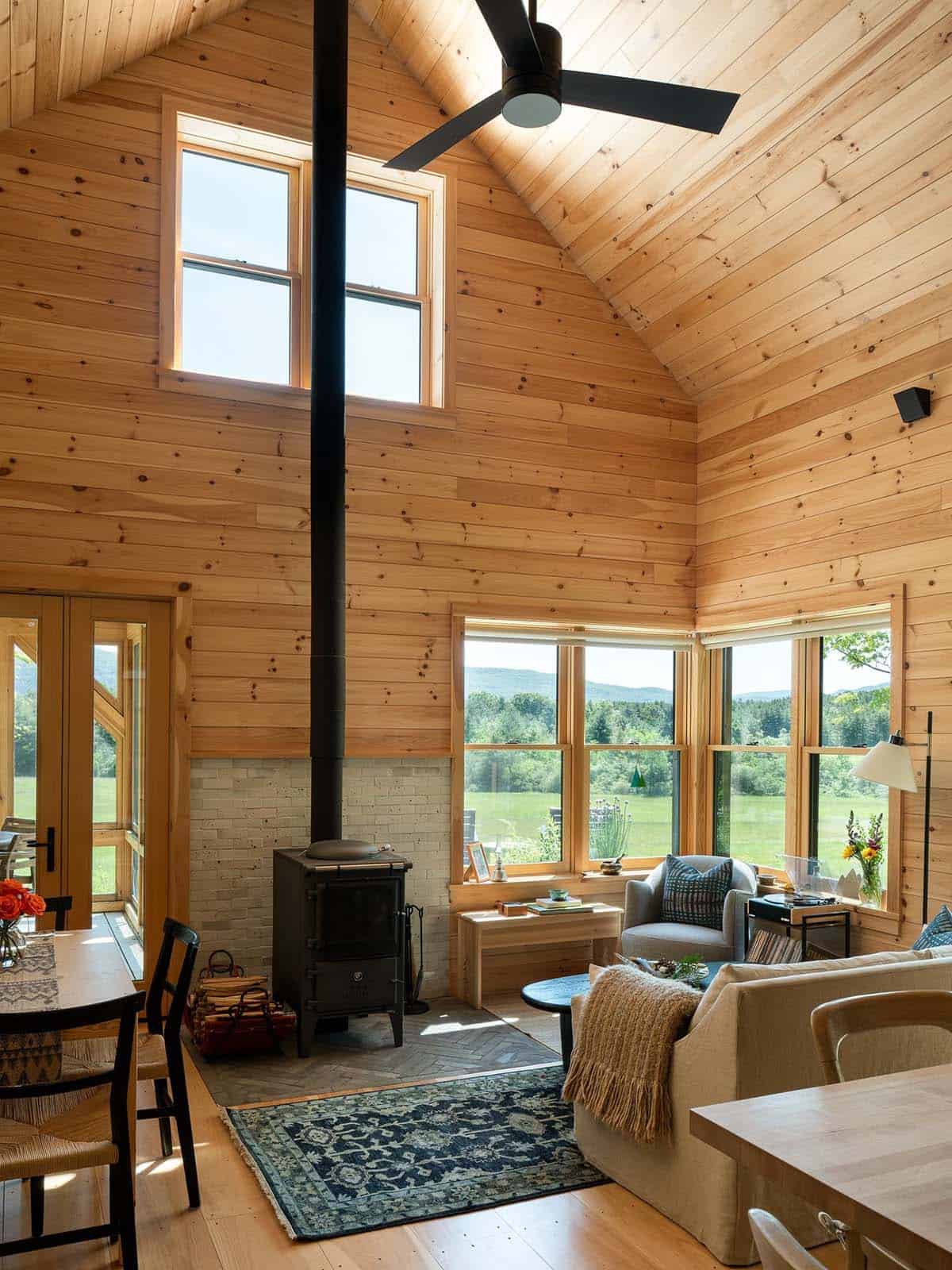 Living area with wood stove, pale brick wall, and vaulted ceiling
