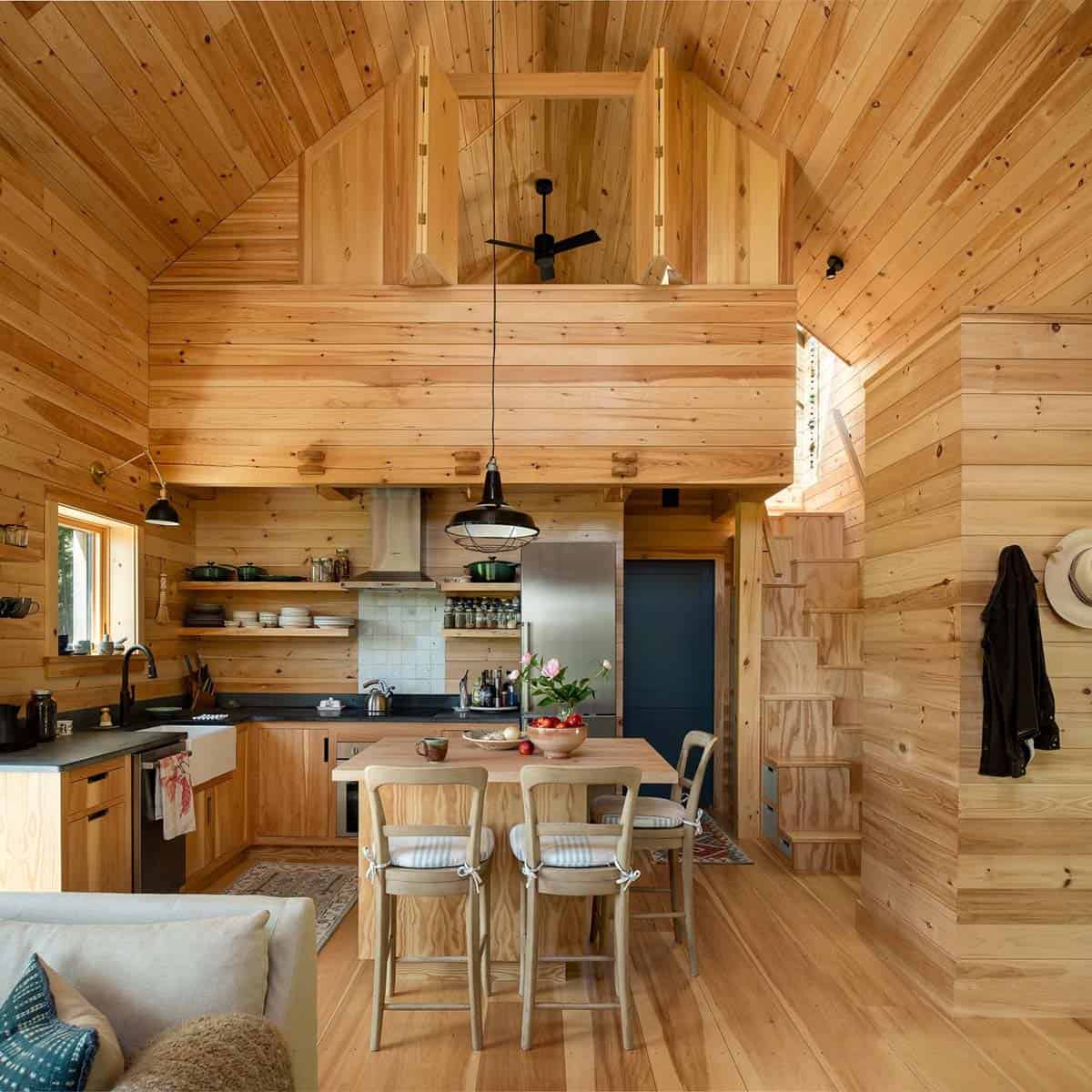 Wood-paneled kitchen with butcher block island, open shelving, and loft above