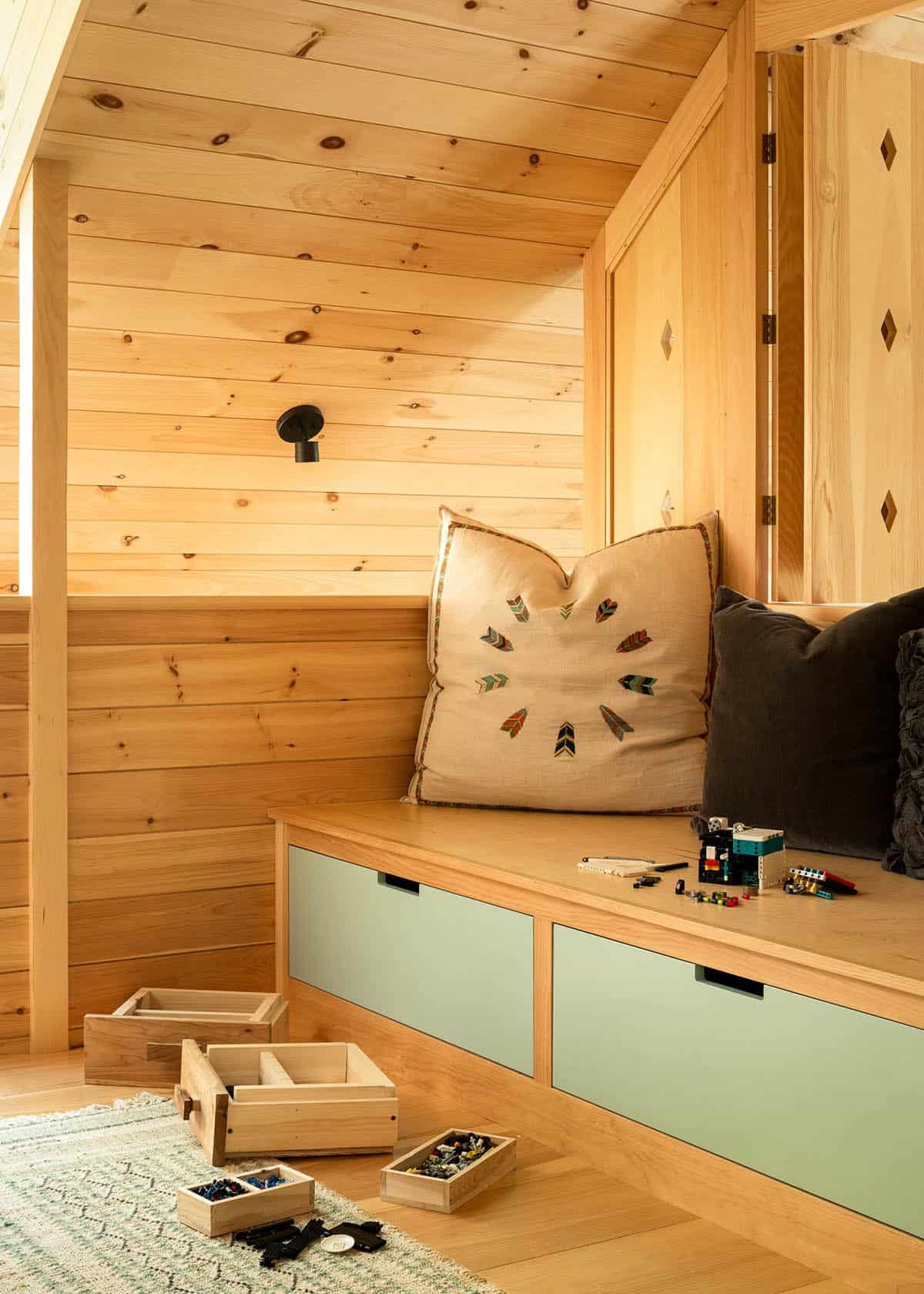 Loft bench with sage green drawers, feather pillow, and wooden storage boxes