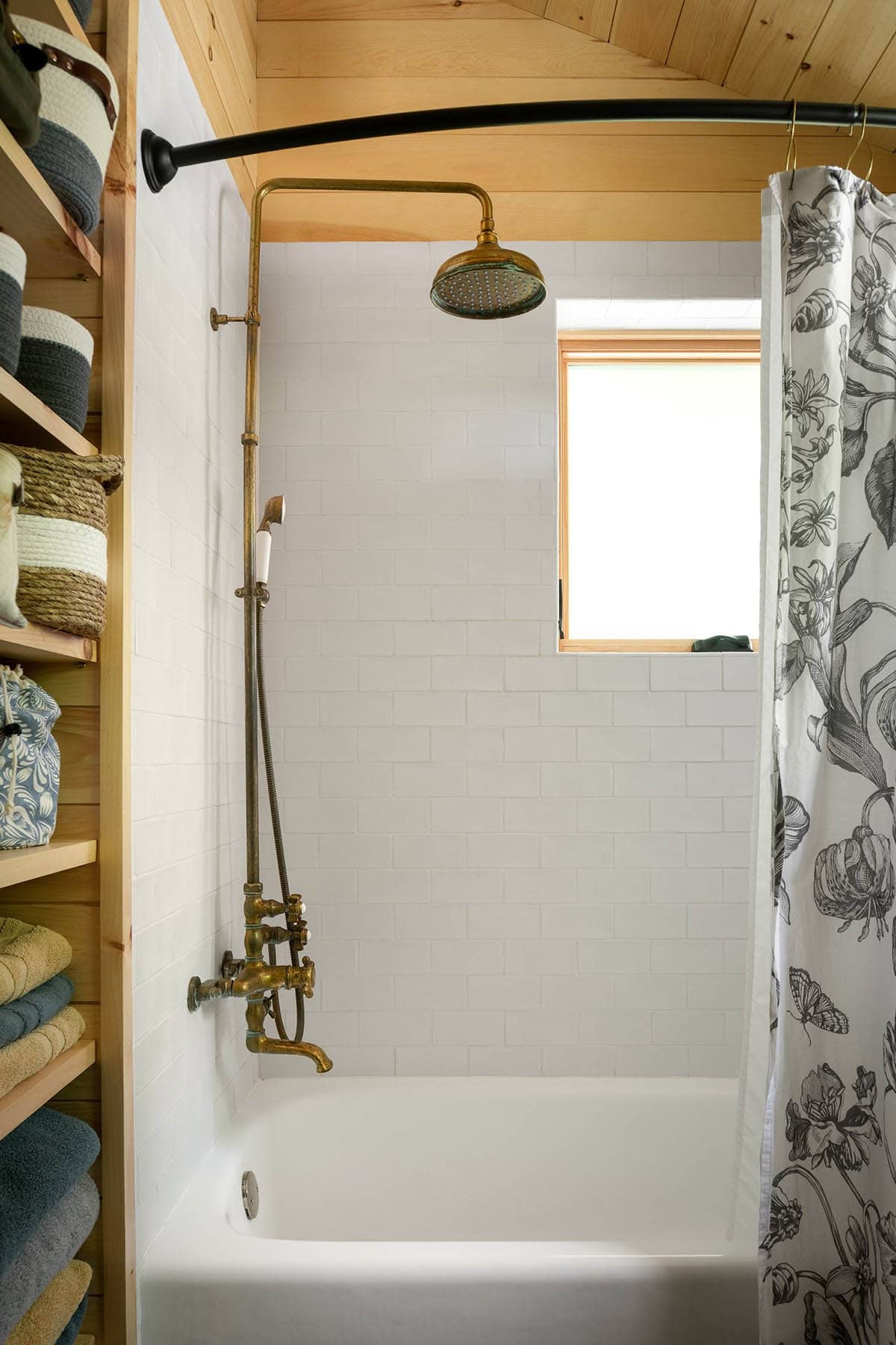 Bathtub shower with white subway tile, exposed brass fixtures, and floral curtain