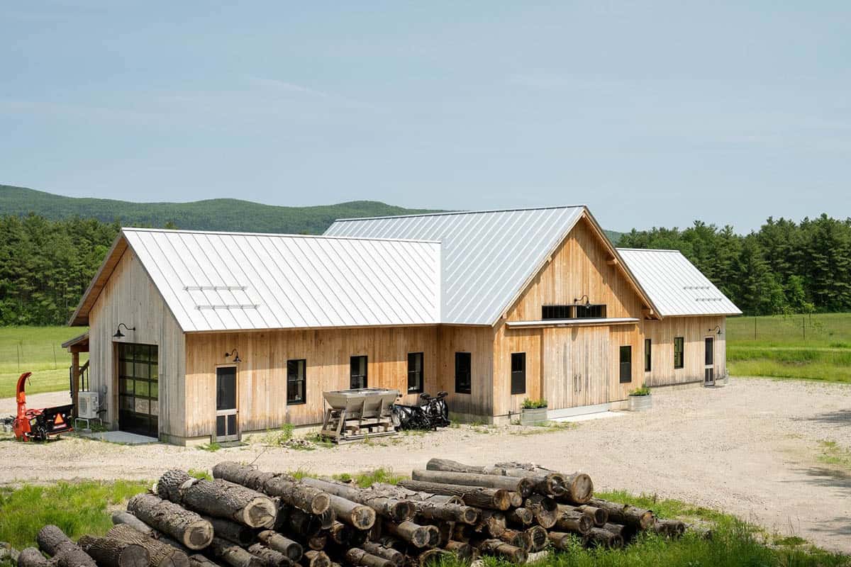 Barn-style outbuilding with metal roof and stacked logs in foreground