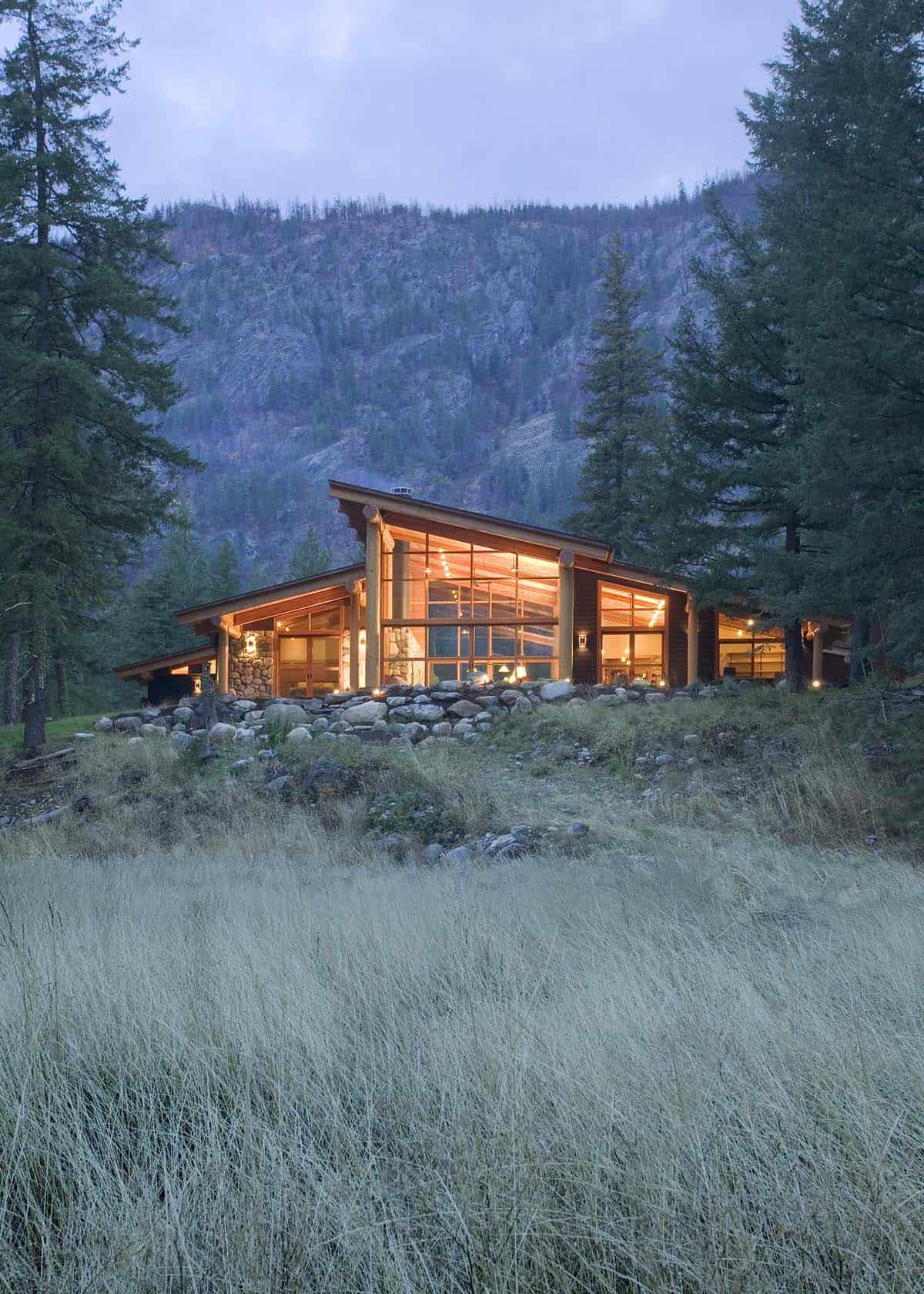 Cabin nestled against rocky cliff with tall meadow grasses foreground
