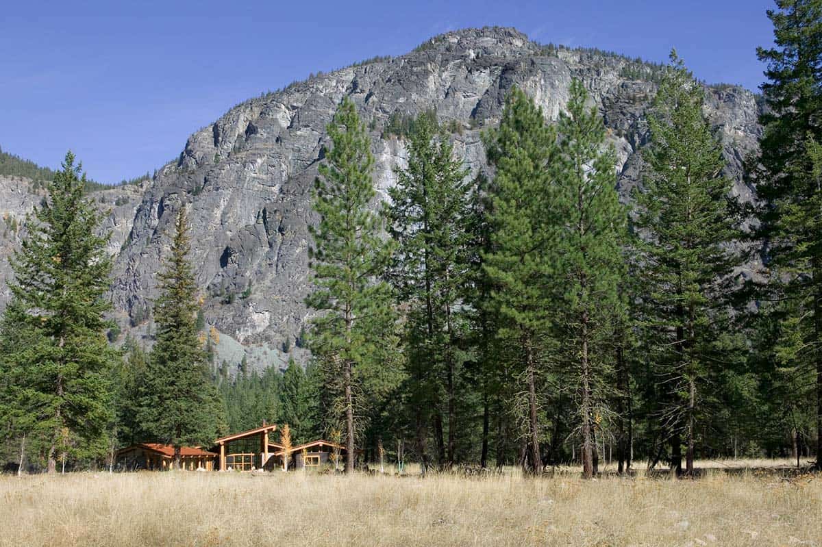 Distant view of cabin dwarfed by towering rock formation and pines
