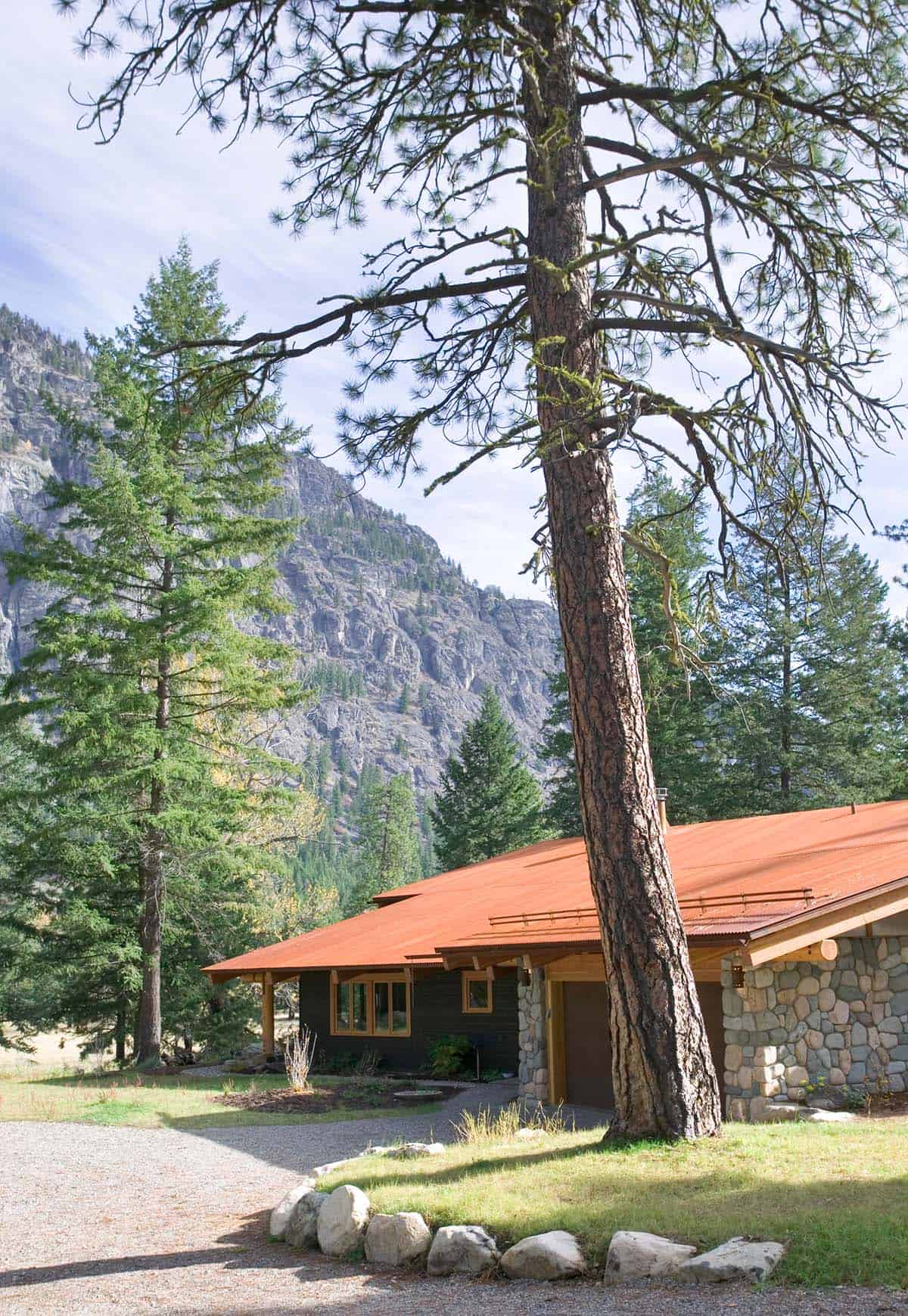 Garage and stone facade beneath towering pine and rocky peak