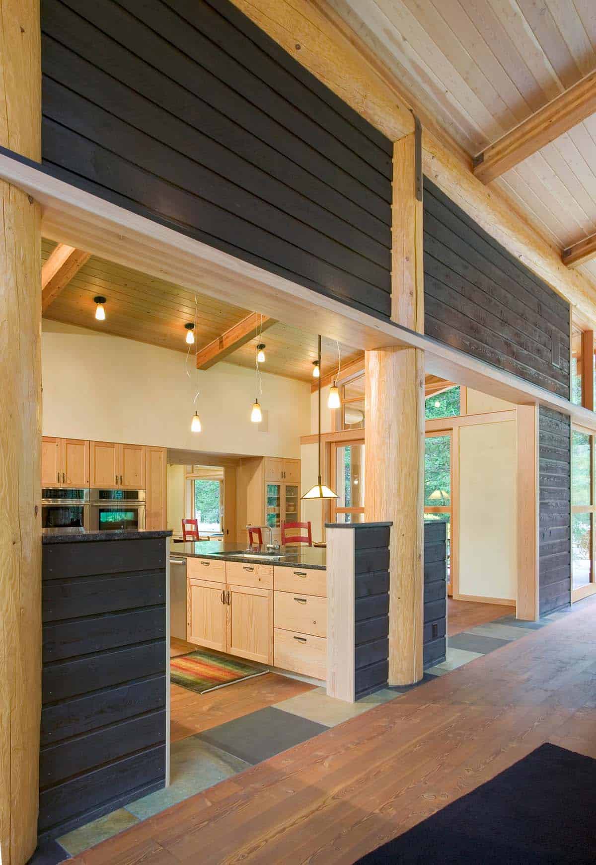 Kitchen view through dark wood accent wall and log columns