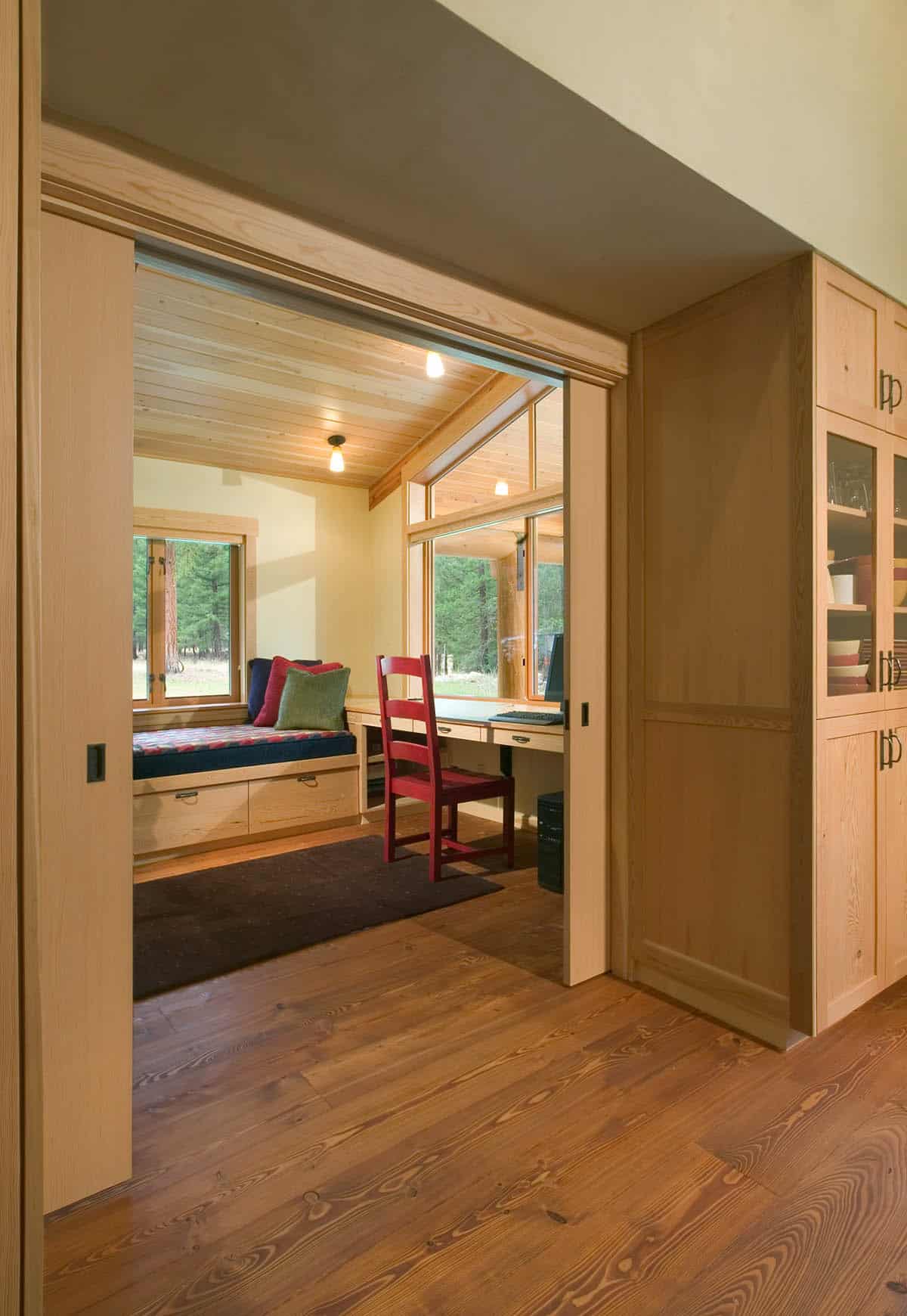 Home office nook with window seat, built-in desk, and red chair