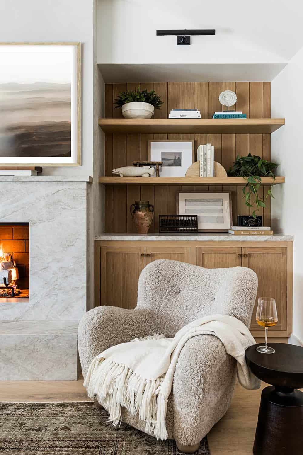 Shearling armchair beside fireplace with styled oak built-in shelving