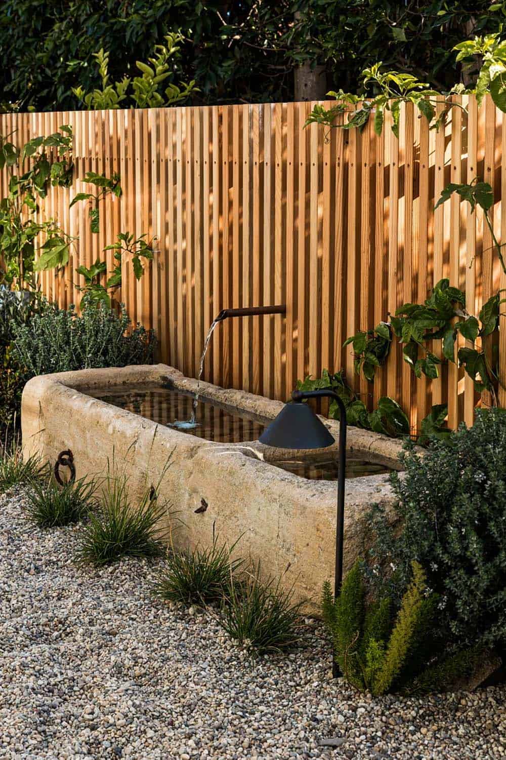 Stone trough fountain against cedar slat privacy fence