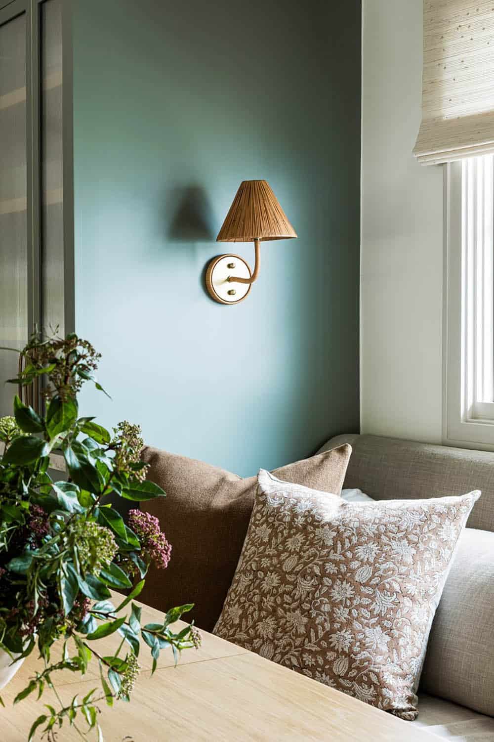 Teal accent wall with rattan sconce and floral throw pillow