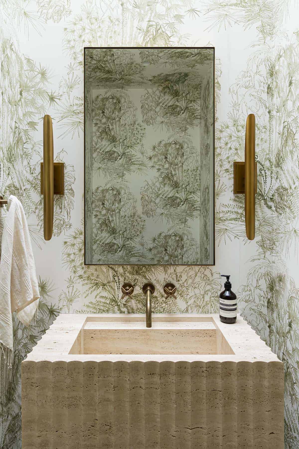 Travertine sink with botanical wallpaper and gold sconces