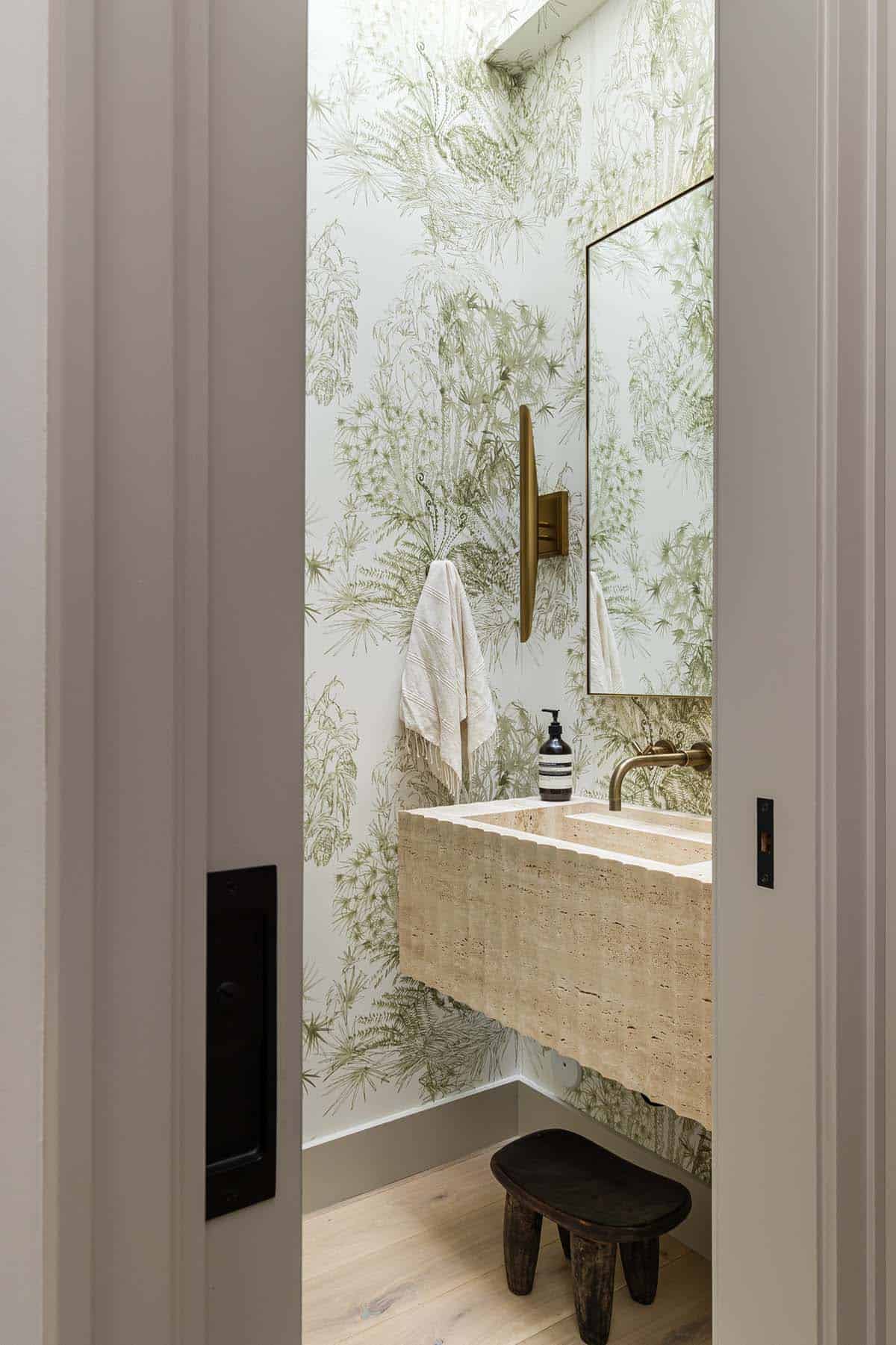 Fluted travertine sink framed by fern-print wallpaper in powder room