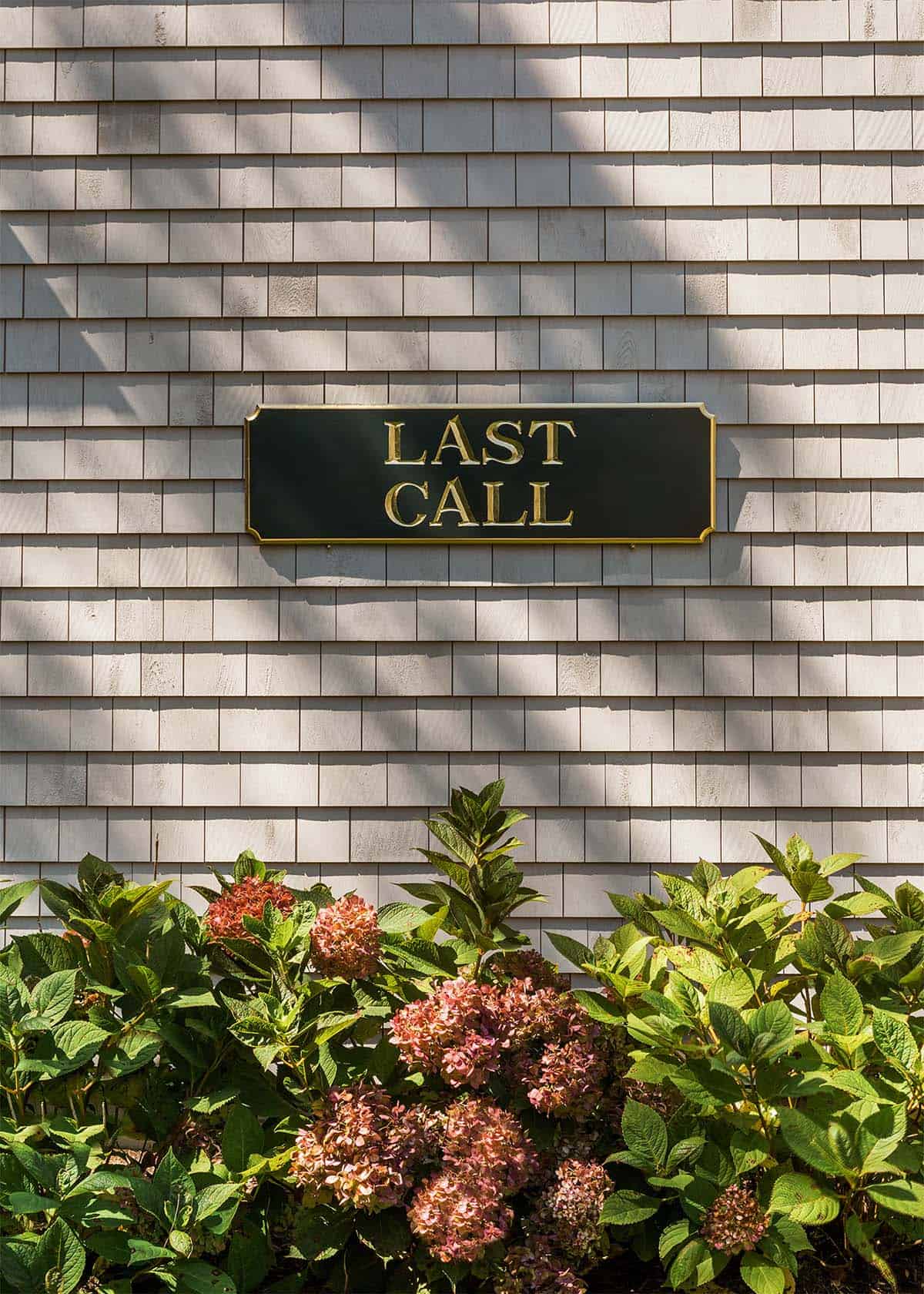 Last Call sign mounted on shingled wall above hydrangeas