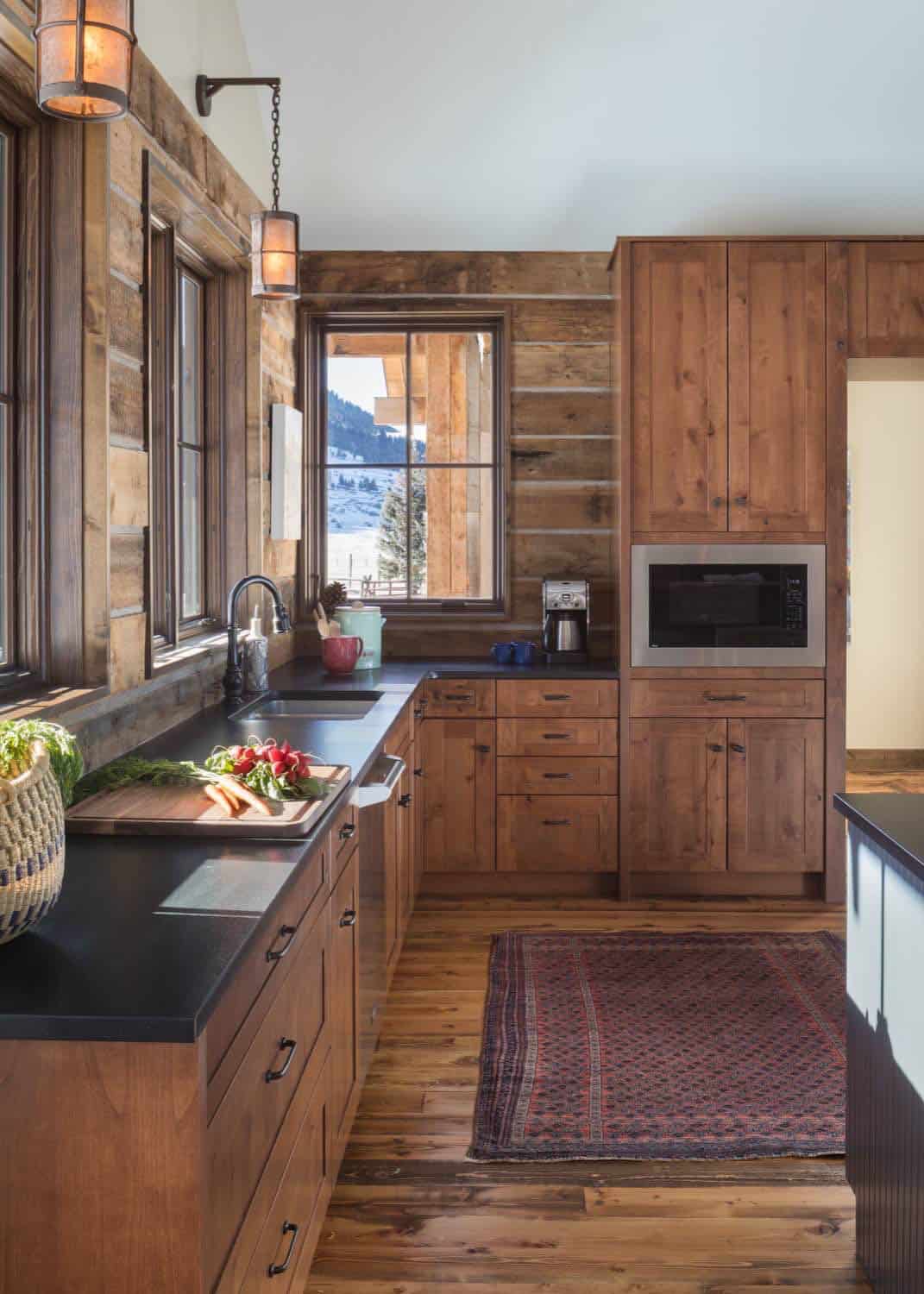 Rustic kitchen with wood cabinetry, black countertops, built-in microwave, and patterned rug