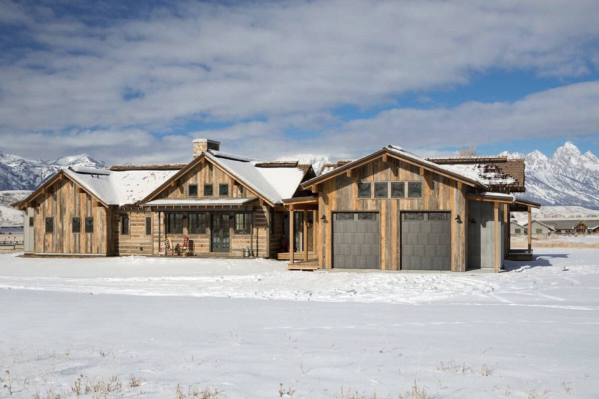 Snow-covered rustic home exterior with attached two-car garage and mountain range backdrop